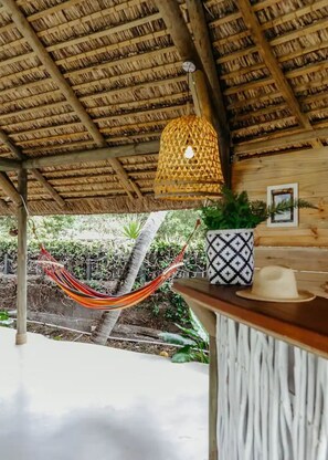A wooden structure with a thatched roof, a hammock, a hanging light fixture, and a potted plant. - Boutik Retreats (Le Morne)