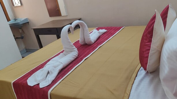 Habitación de hotel con cama, un arreglo de toallas rojo y blanco, y una mesita de noche de madera.