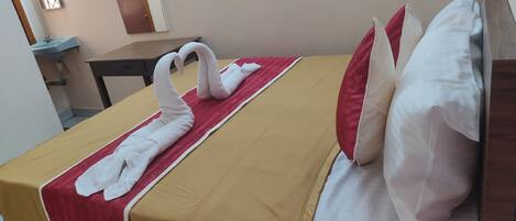 Habitación de hotel con cama, un arreglo de toallas rojo y blanco, y una mesita de noche de madera.