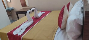 A hotel room with a bed, a red and white towel arrangement, and a wooden nightstand.