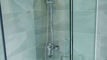 A glass-enclosed shower with a handheld showerhead and a wall-mounted faucet.