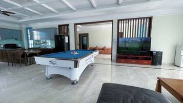 A spacious living area with a pool table, a sofa, a TV, and a kitchen area.
