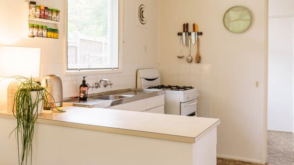 A kitchen with a sink, stove, and hanging utensils. - Rosie's Place l Point Lonsdale (Point Lonsdale)