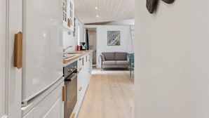 A modern kitchen with white cabinets, a wooden countertop, and a built-in oven. There is a dining area with a sofa and a painting on the wall. - Cozy retreat near the Djursland coast (Ørsted)