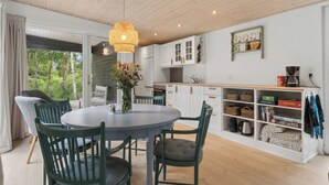 A modern kitchen with white cabinets, a dining table with chairs, a hanging light fixture, and a view of trees outside. - Cozy retreat near the Djursland coast (Ørsted)