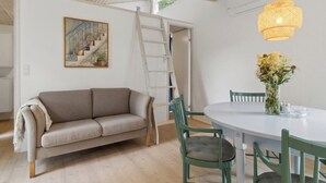 A room with a sofa, dining table, chairs, a ladder, and a hanging light fixture. - Cozy retreat near the Djursland coast (Ørsted)