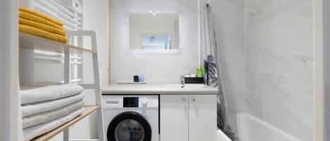 Une petite salle de bain équipée d’un lave-linge, d’un évier et d’une douche.