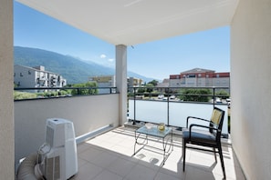 A balcony with a table and chair, an air conditioning unit, and a view of buildings and mountains.