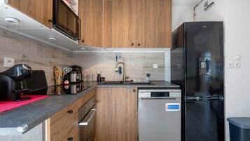 Une cuisine de taille réduite, dotée de meubles en bois, d’un lave-vaisselle en acier inoxydable et d’un réfrigérateur noir.