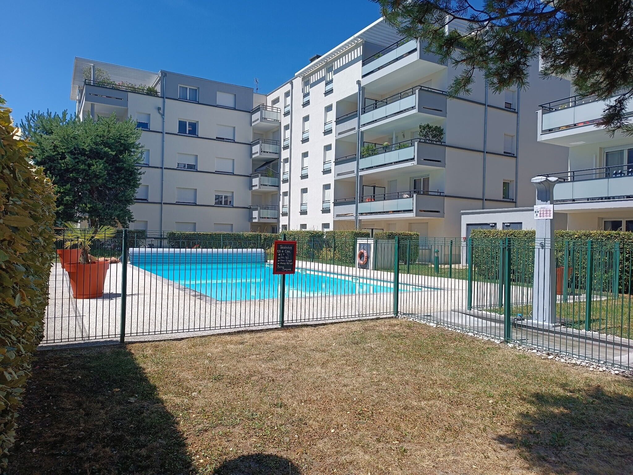 Un immeuble résidentiel doté d’une piscine, entouré d’une clôture et de verdure.