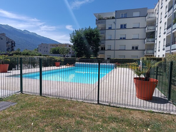 A swimming pool surrounded by a fence, with buildings and mountains in the background.