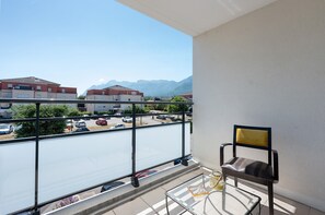 A balcony with a glass table, a chair, and a view of a parking lot and buildings in the background.