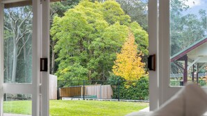 Vista attraverso una porta di vetro su un giardino con alberi e una recinzione.