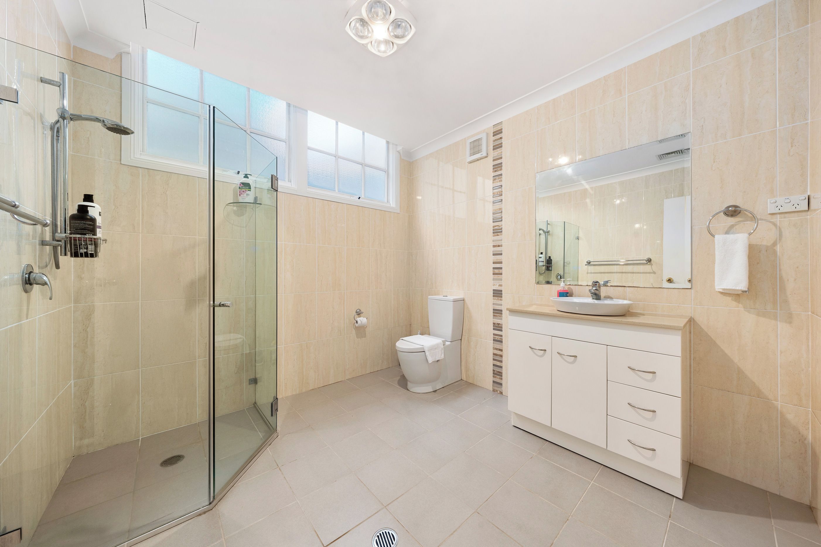 A modern bathroom with a glass shower enclosure, a toilet, a sink with a mirror, and a vanity with drawers.