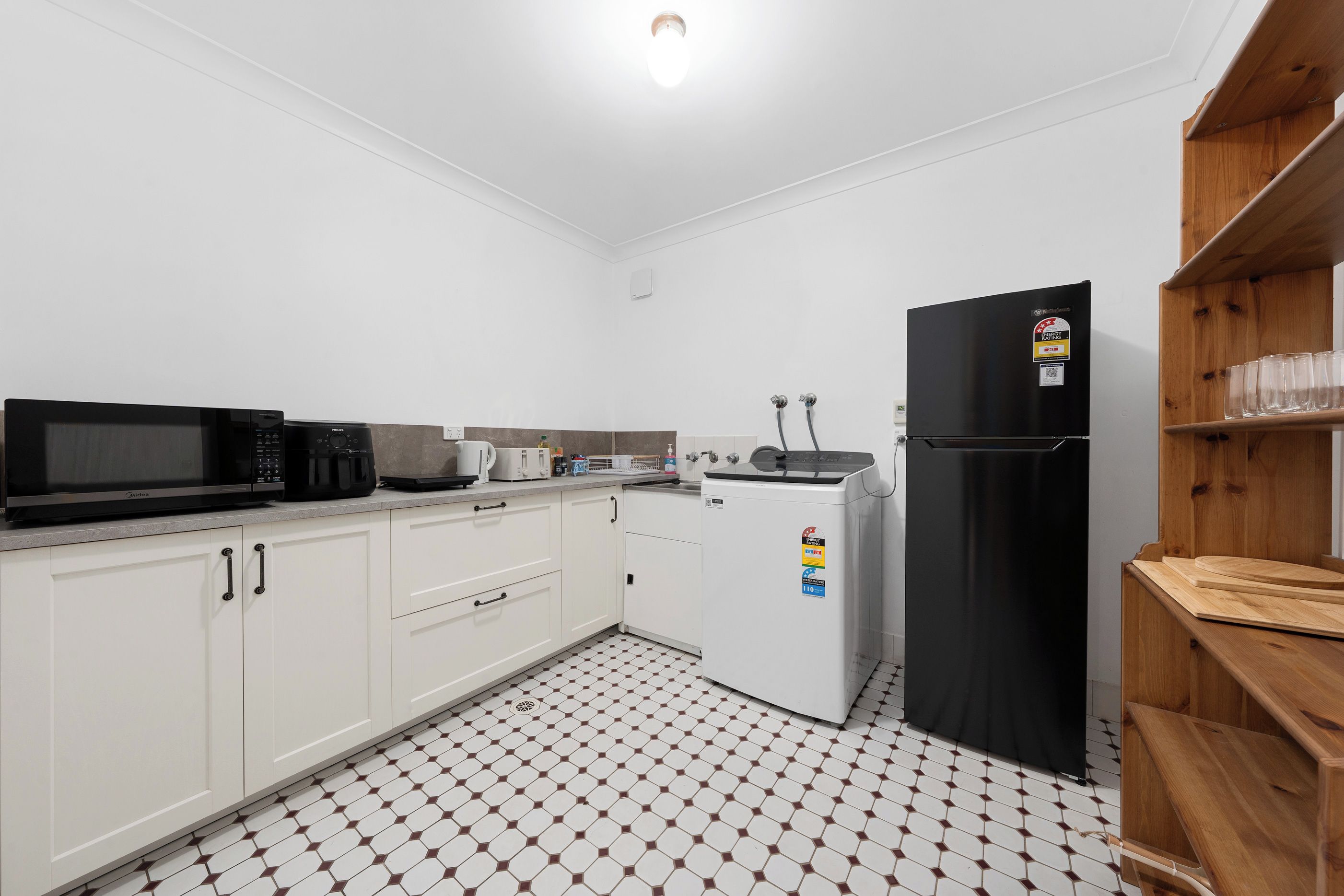 A compact kitchen with white cabinets, a black refrigerator, a microwave, a toaster, and a coffee maker.