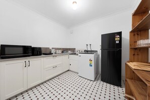 A compact kitchen with white cabinets, a black refrigerator, a microwave, a toaster, and a coffee maker.