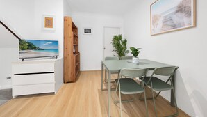 Una camera moderna con TV a schermo piatto, un tavolo da pranzo con sedie, una libreria in legno e una pianta in vaso.