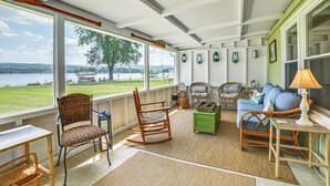 A cozy room with wicker furniture, a rocking chair, a blue sofa, and a view of a lake. - 2 Lamoka Lake Cottages w/ Views, Fire Pit & Dock (Bradford)