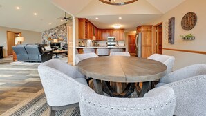 A dining area with a round table and upholstered chairs, a kitchen with wooden cabinets, and a stone accent wall. - Spacious Lake Arrowhead Home on the Golf Course (Nekoosa)
