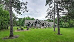 A large house with a stone foundation, a lawn, and a patio with chairs. - Spacious Lake Arrowhead Home on the Golf Course (Nekoosa)