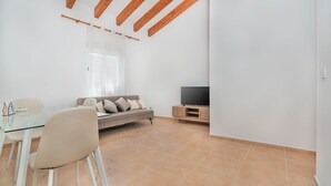 Een moderne woonkamer met een glazen eettafel, een beige bank en een flatscreen televisie op een houten dressoir.