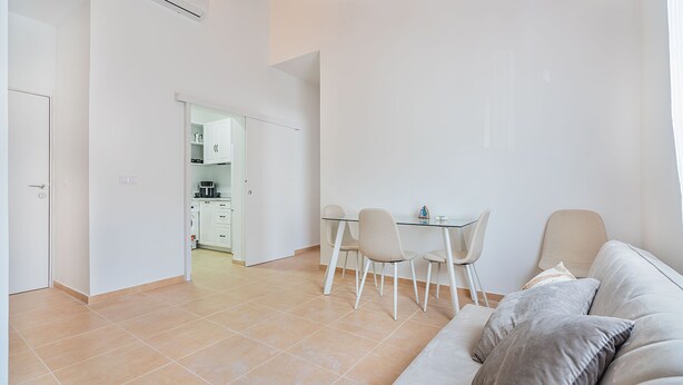 Een moderne woonkamer met een bank, een eettafel met stoelen, en een keuken op de achtergrond.