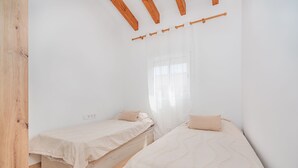 Een slaapkamer met twee eenpersoonsbedden, houten balken in het plafond, een raam met dunne gordijnen en een betegelde vloer.