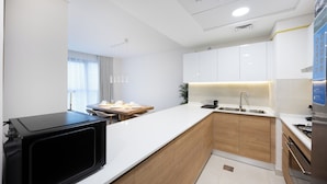Une cuisine moderne avec des meubles blancs, un micro-ondes noir, un plan de travail en bois et un évier.