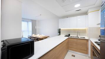Une cuisine moderne avec des meubles blancs, un micro-ondes noir, un plan de travail en bois et un évier.