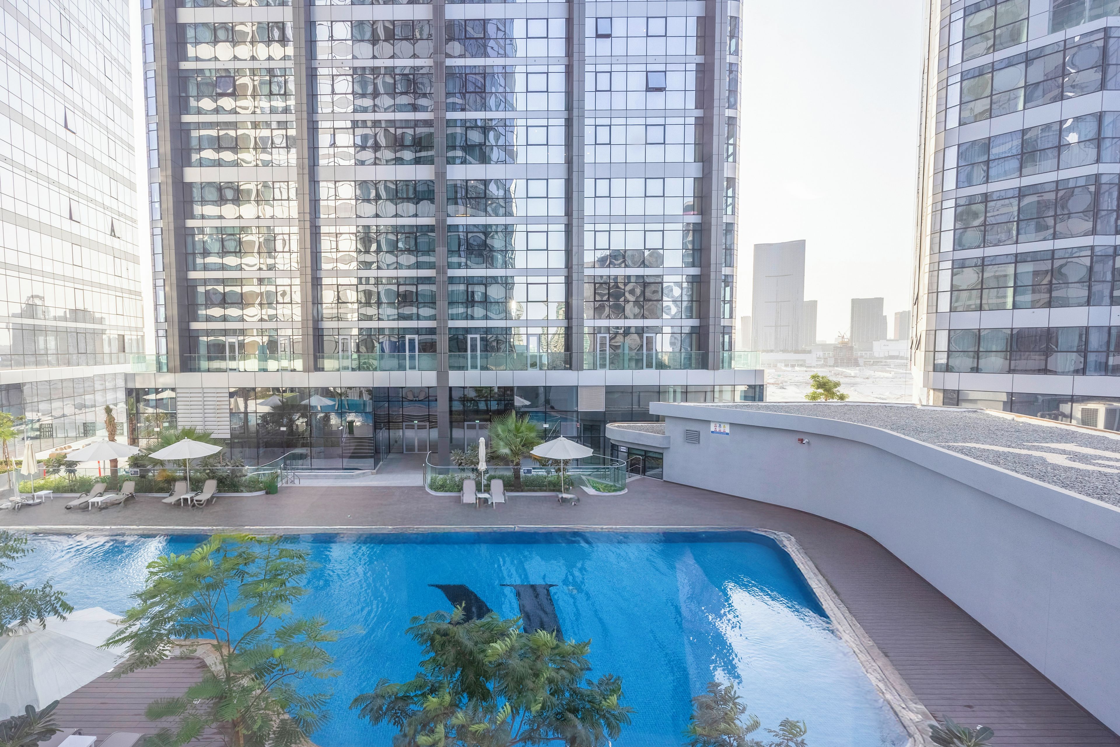 A modern building with a rooftop pool surrounded by lounge chairs and umbrellas.