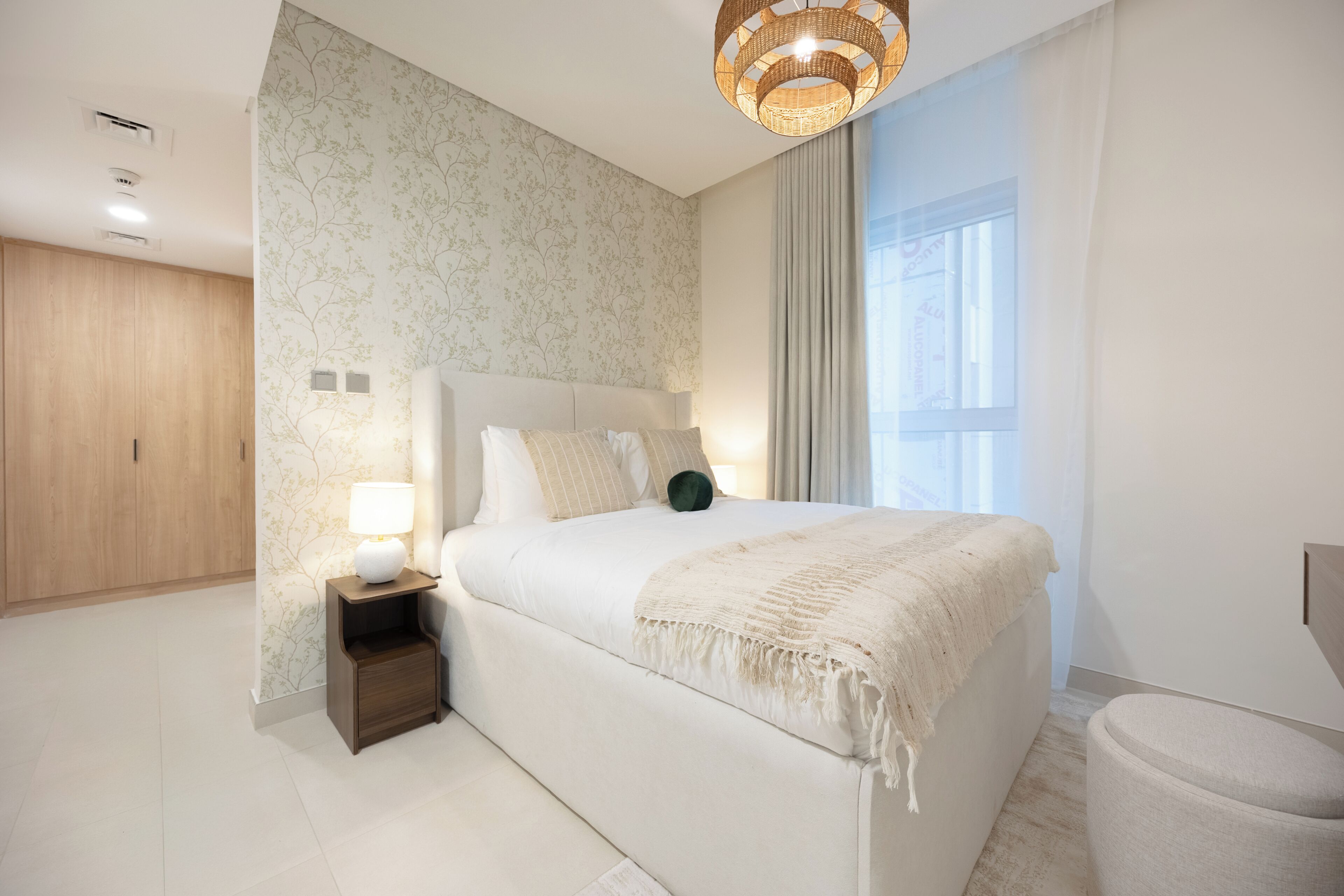 Un dormitorio con cama, mesita de noche, lámpara y ventana con cortinas.