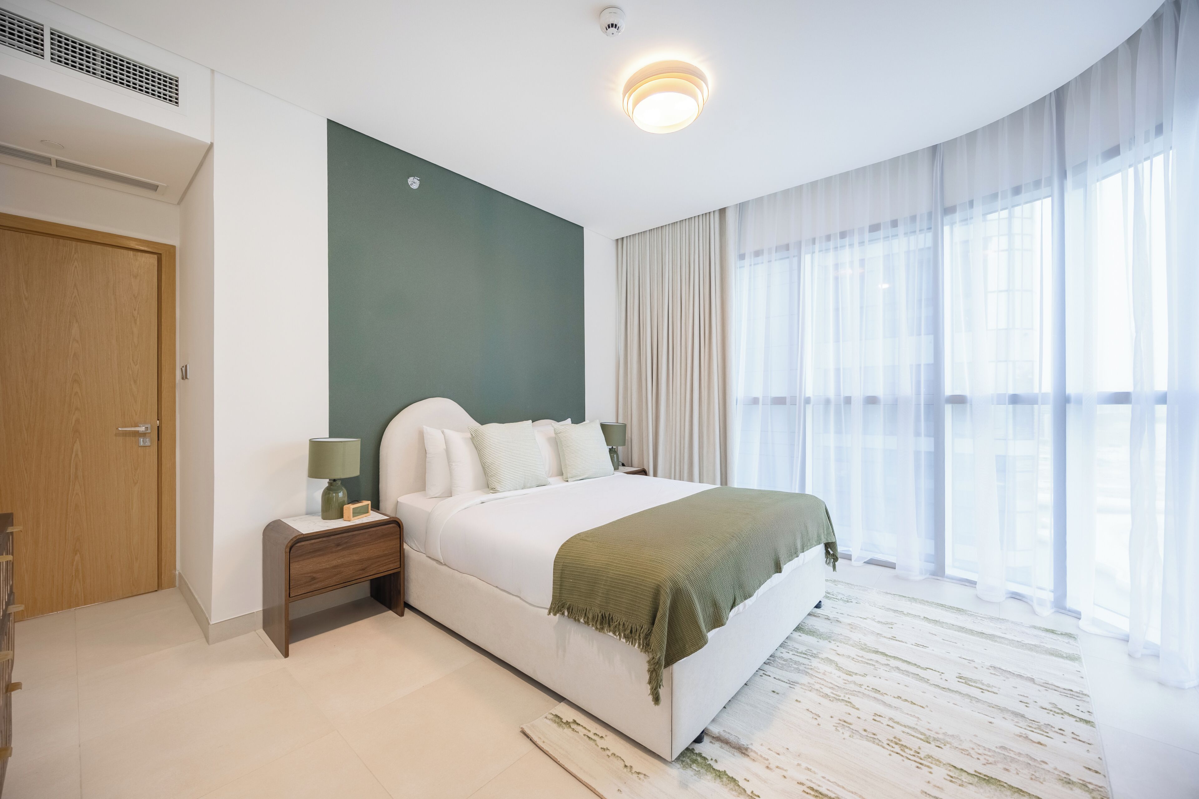 A bedroom with a bed, nightstand, lamp, and curtains.