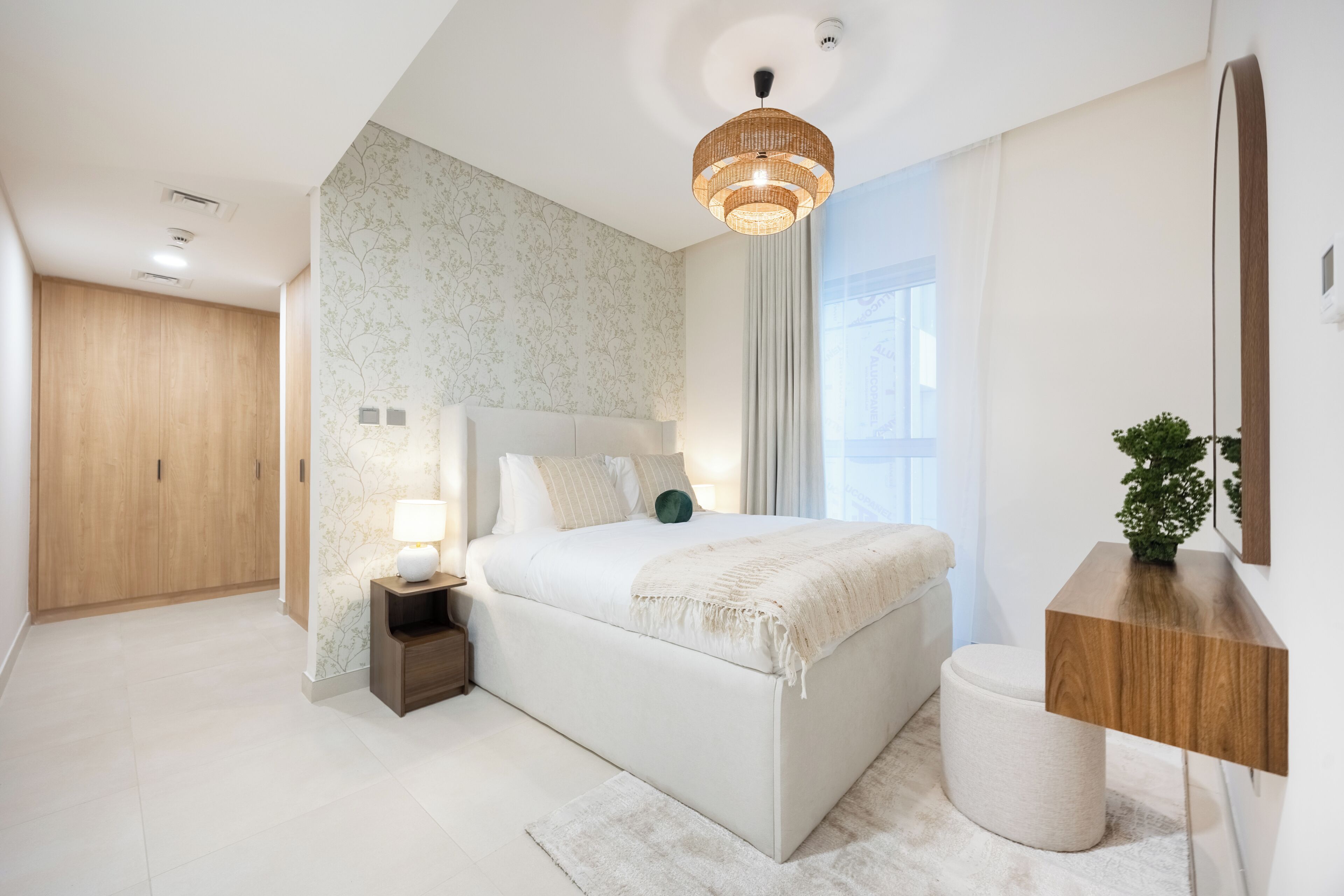 A modern bedroom with a large bed, bedside table, nightstand, and a mirror on the wall.