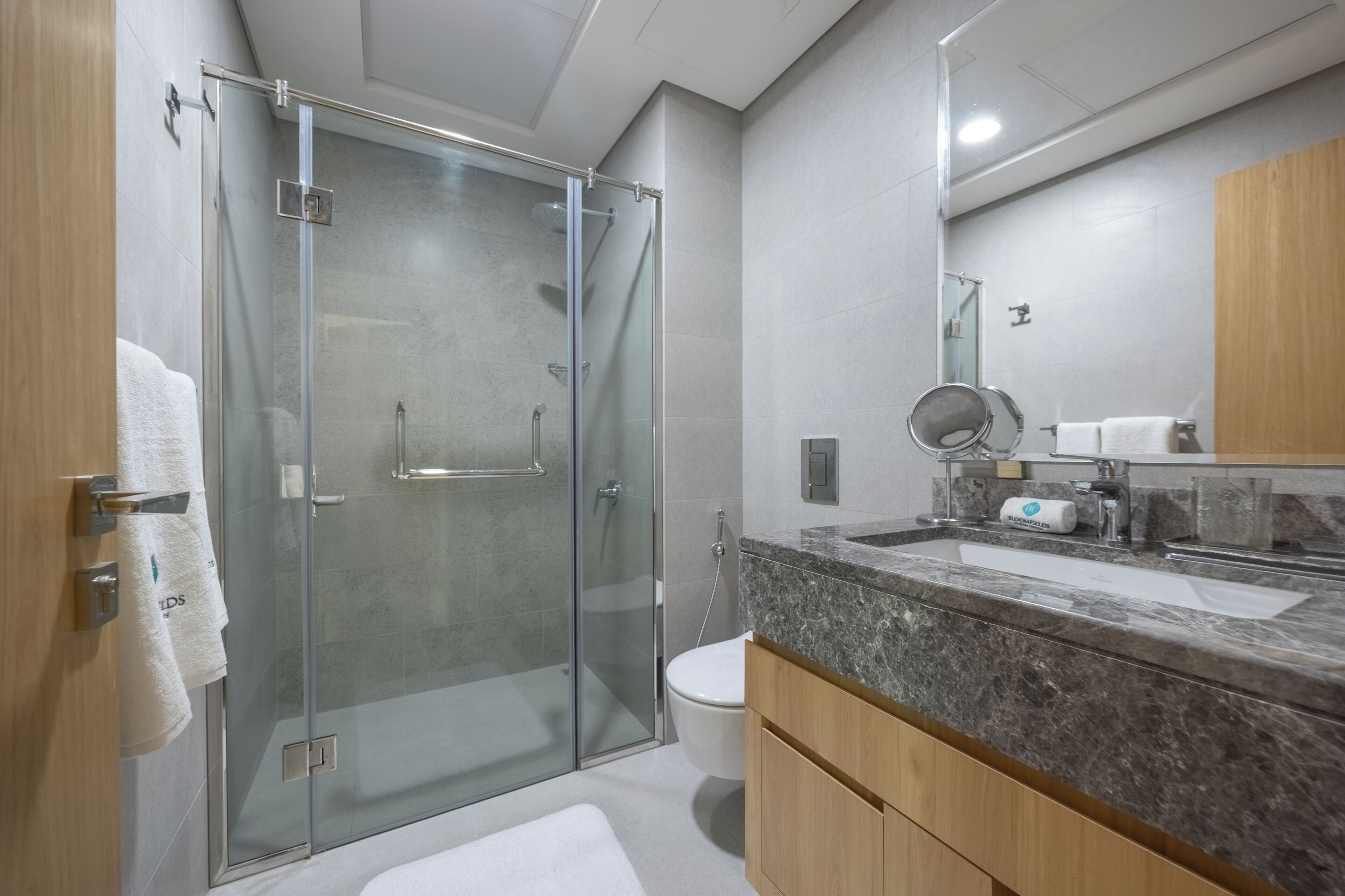 Ein modernes Badezimmer mit Duschkabine aus Glas, Toilette, Waschbecken mit Marmorplatte und Holzschränken.