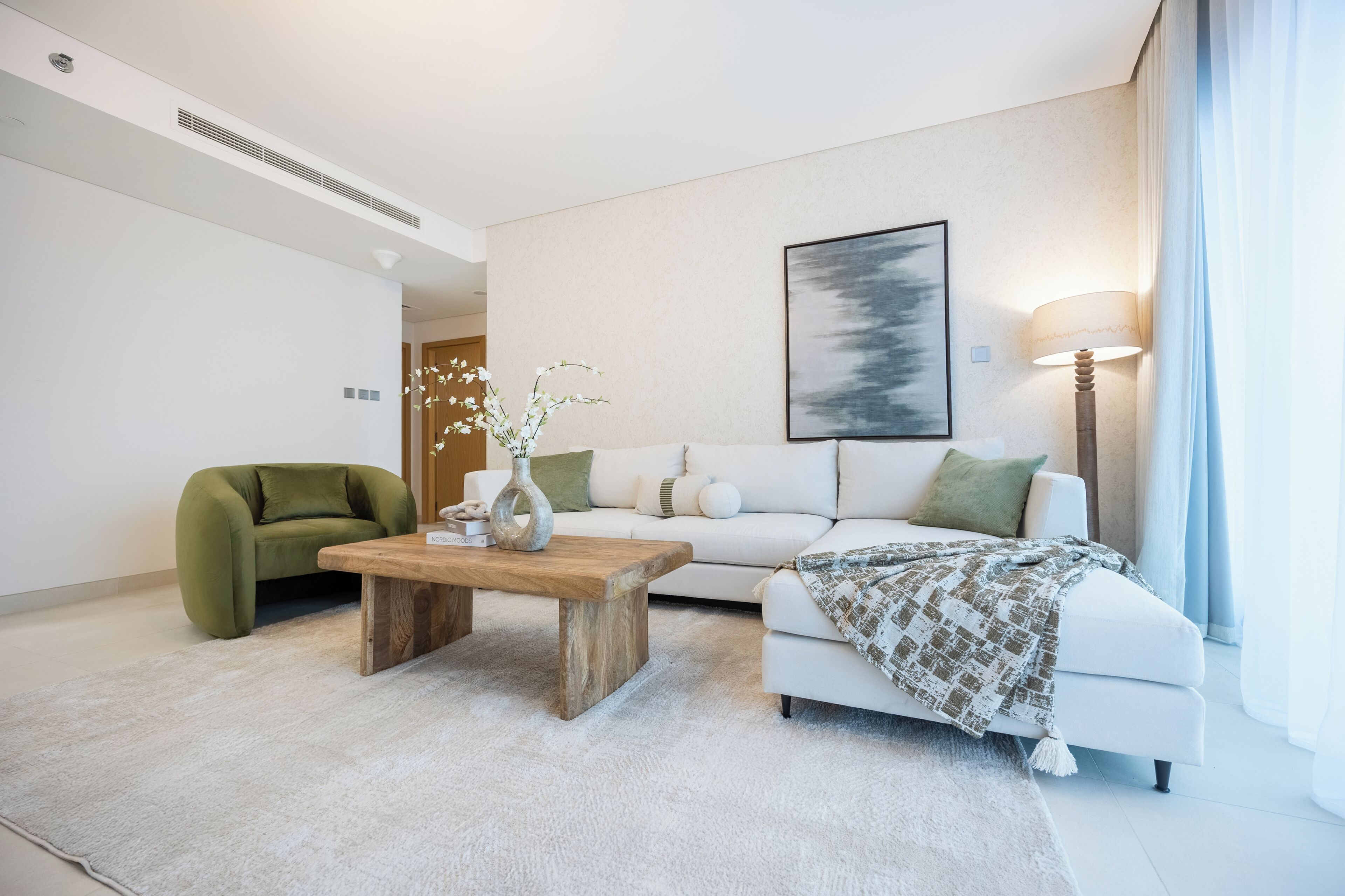 A modern living room with a sofa, a green armchair, a wooden coffee table, a floor lamp, and a painting on the wall.
