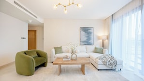 Un salon moderne avec un canapé, un fauteuil vert, une table basse et un lustre.