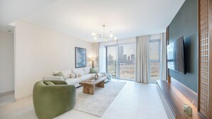 Un salon moderne avec un canapé, un fauteuil vert, une table basse en bois et un téléviseur posé sur un meuble en bois.