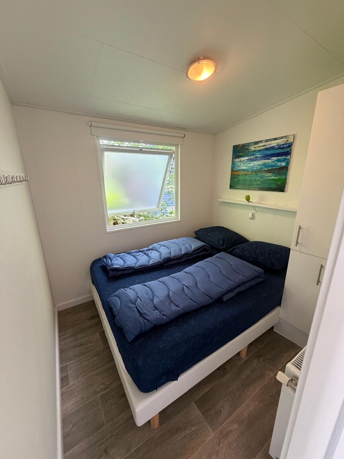 Una habitación pequeña con cama individual, ventana, un cuadro y un radiador.