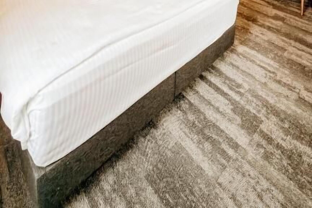A hotel room with a large bed, a desk, a chair, a wardrobe, and a hanging light fixture.