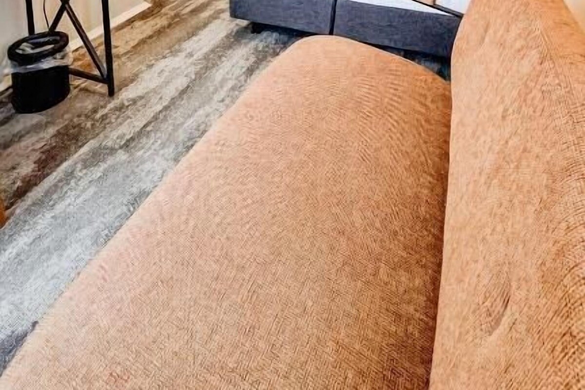 A hotel room with a bed, a sofa, a desk with a mirror, and a wardrobe.