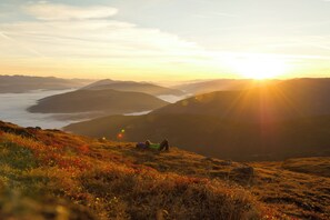 A mountainous landscape with a person lying on the grass during sunset.