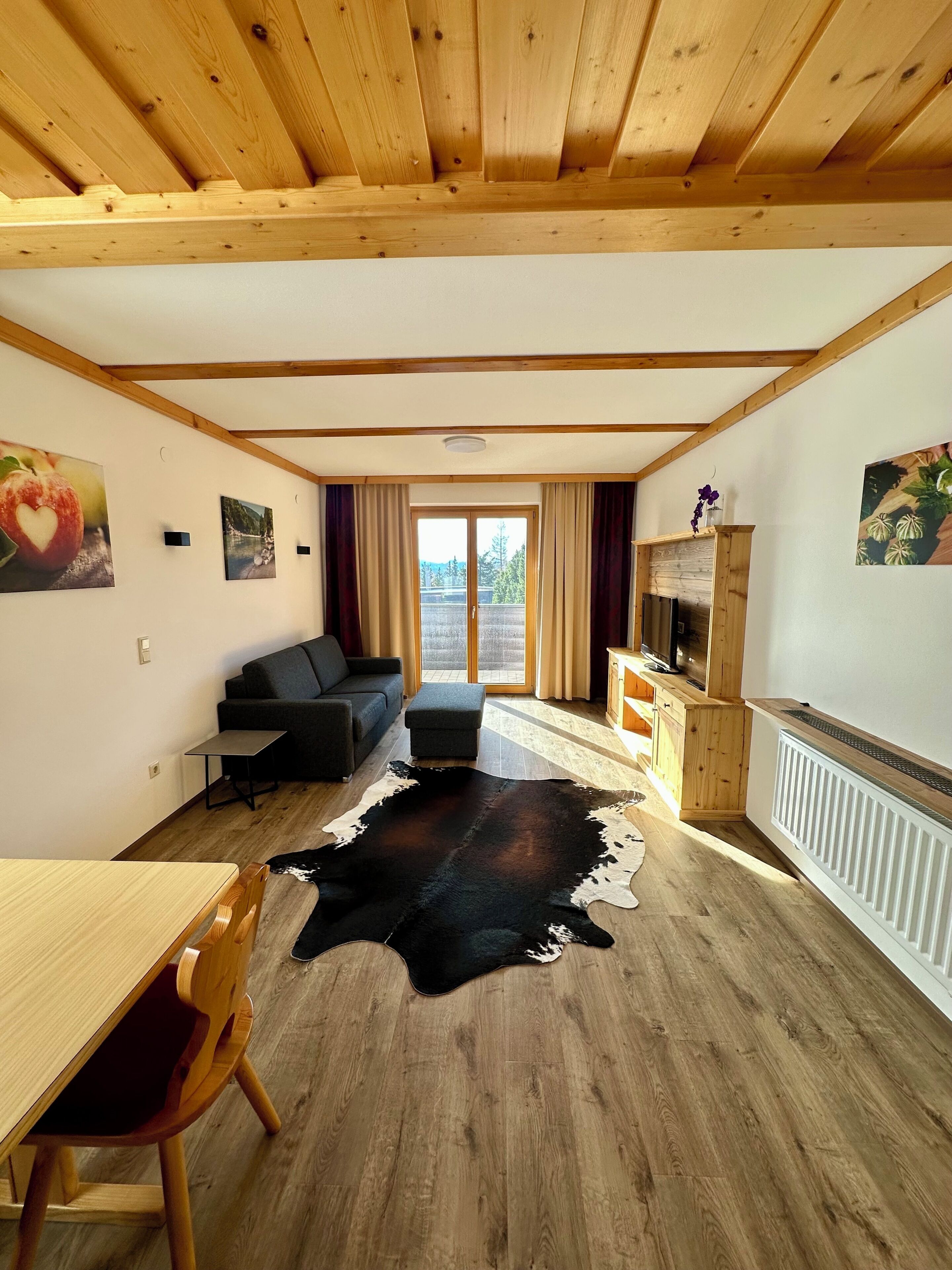 Een kamer met een houten plafond, een bank, een eettafel, een kleden van runderleer en een open haard.