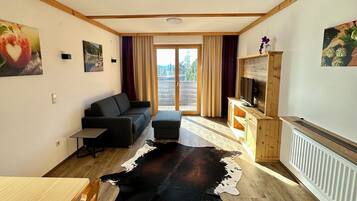 Een kamer met een houten plafond, een bank, een eettafel, een kleden van runderleer en een open haard.