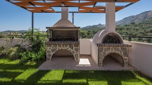 Een buitenkeuken met stenen ovens, een pergola en uitzicht op heuvels.