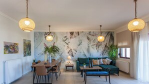 Een ruime woonkamer met een eethoek, een groene bank en een groot wanddecor.