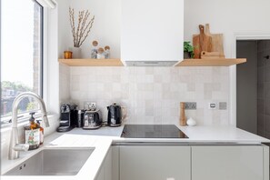 Eine moderne Küche mit weißen Schränken, einer Edelstahl-Spüle, einer Kaffeemaschine, einem Wasserkocher und einem Toaster.