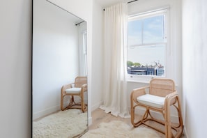 A room with two wicker chairs, a large mirror, and a window with white curtains. - Sleek Scandi Inspired 2BDR Flat inFulham (London)