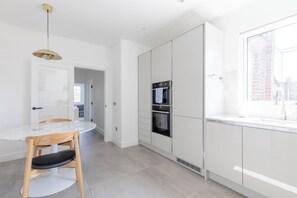 A modern kitchen with white cabinetry, a built-in oven, and a window overlooking a brick wall. - Sleek Scandi Inspired 2BDR Flat inFulham (London)