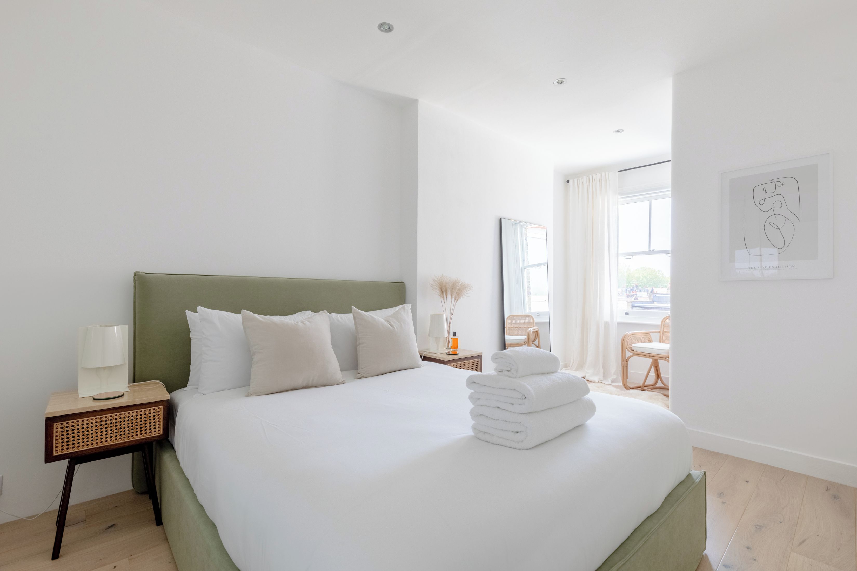 Ein Hotelzimmer mit einem großen Bett, einem Nachttisch mit Lampe, einem Sessel und einem Fenster mit Vorhängen.