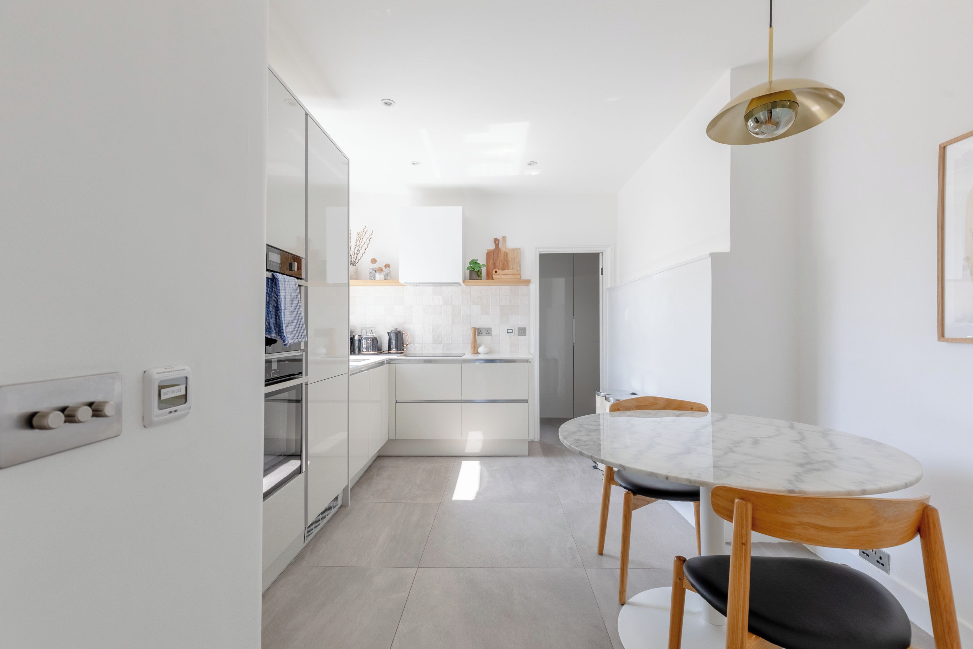 A modern kitchen with white cabinetry, a marble countertop, and a dining area with a round table and wooden chairs.
